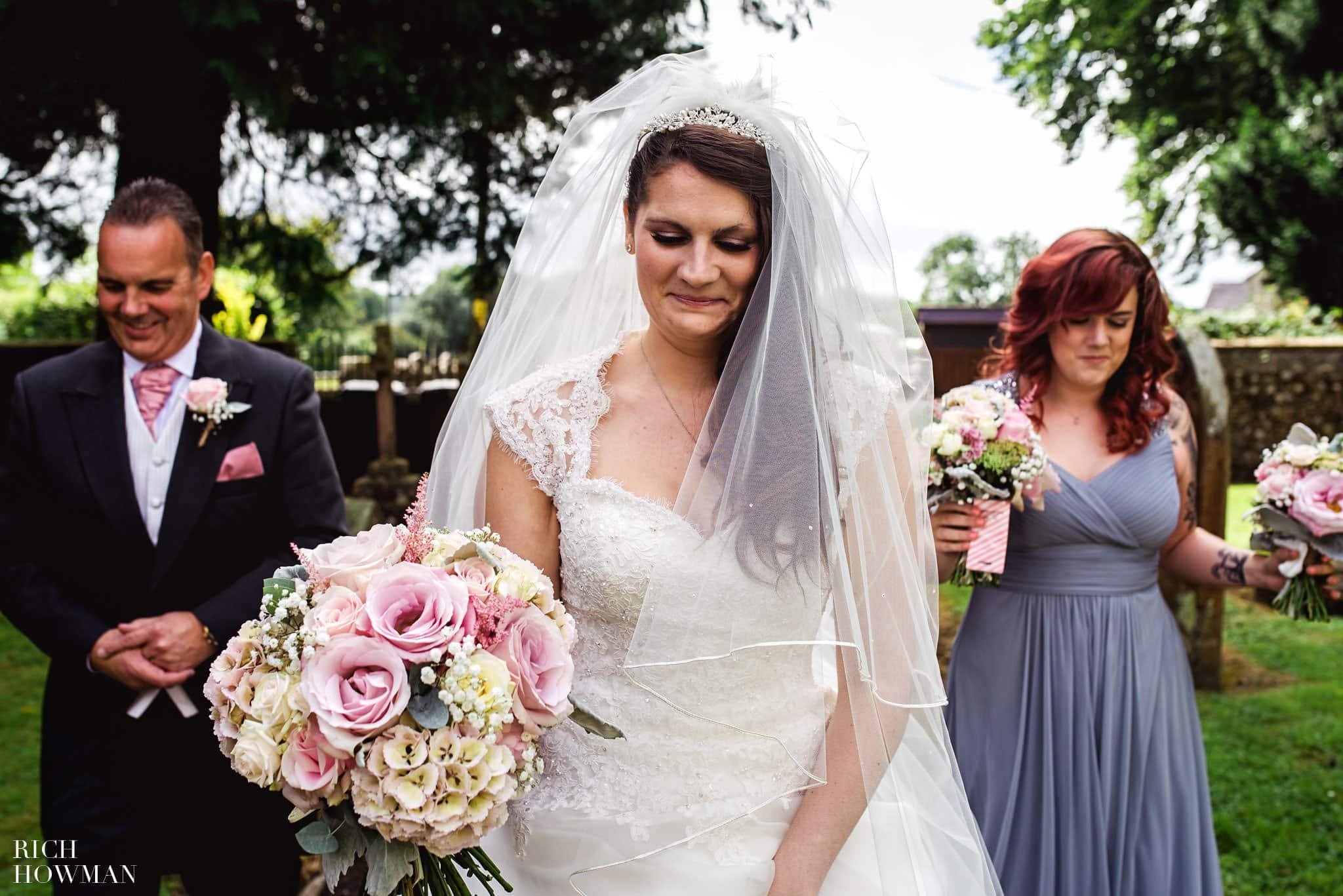 Approaching the church door for her traditional wedding ceremony, the Bride her father and a bridesmaid walk along the path towards the Church