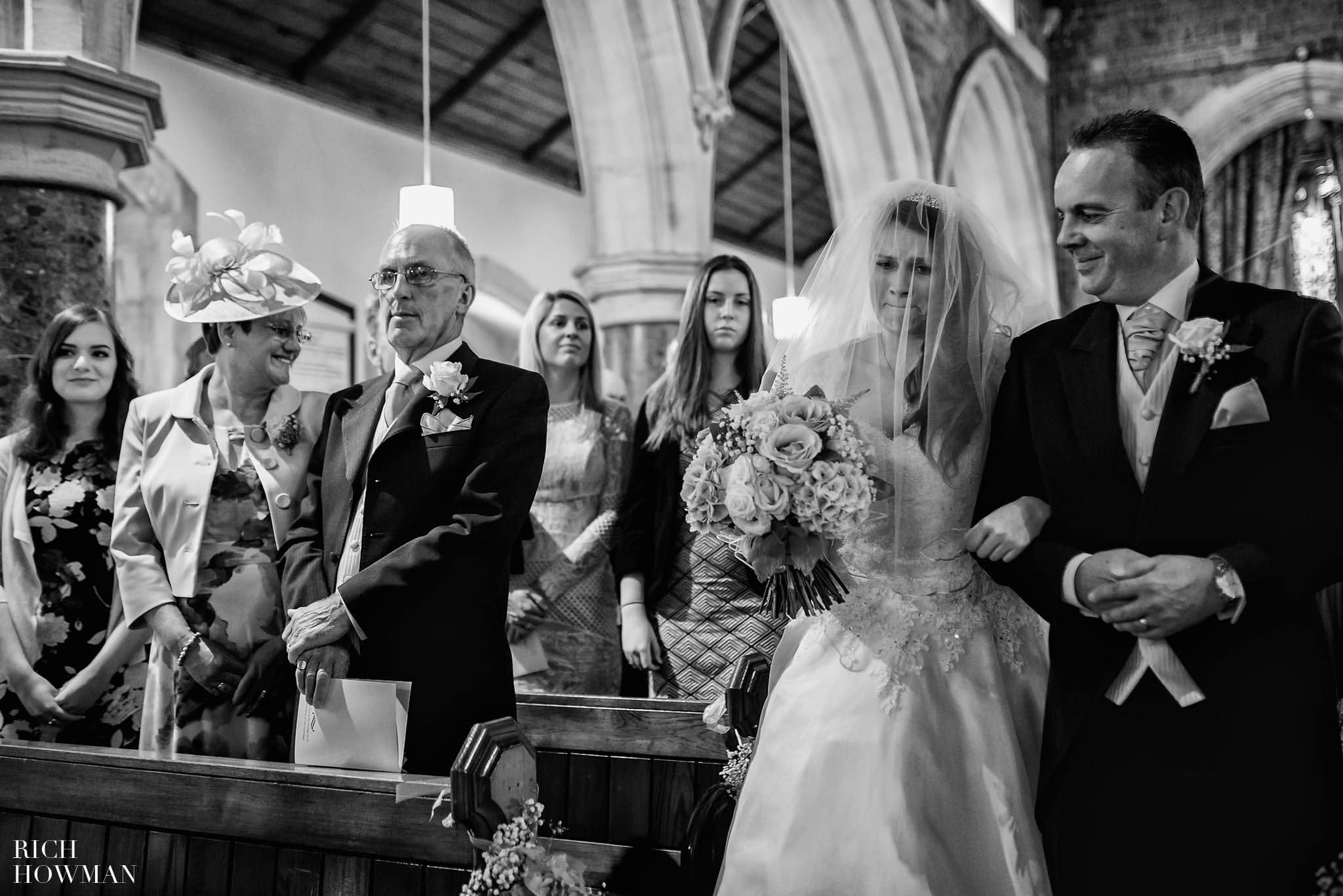 Documentary wedding photo of the bride walking up the aisle in church to meet her waiting fiancée