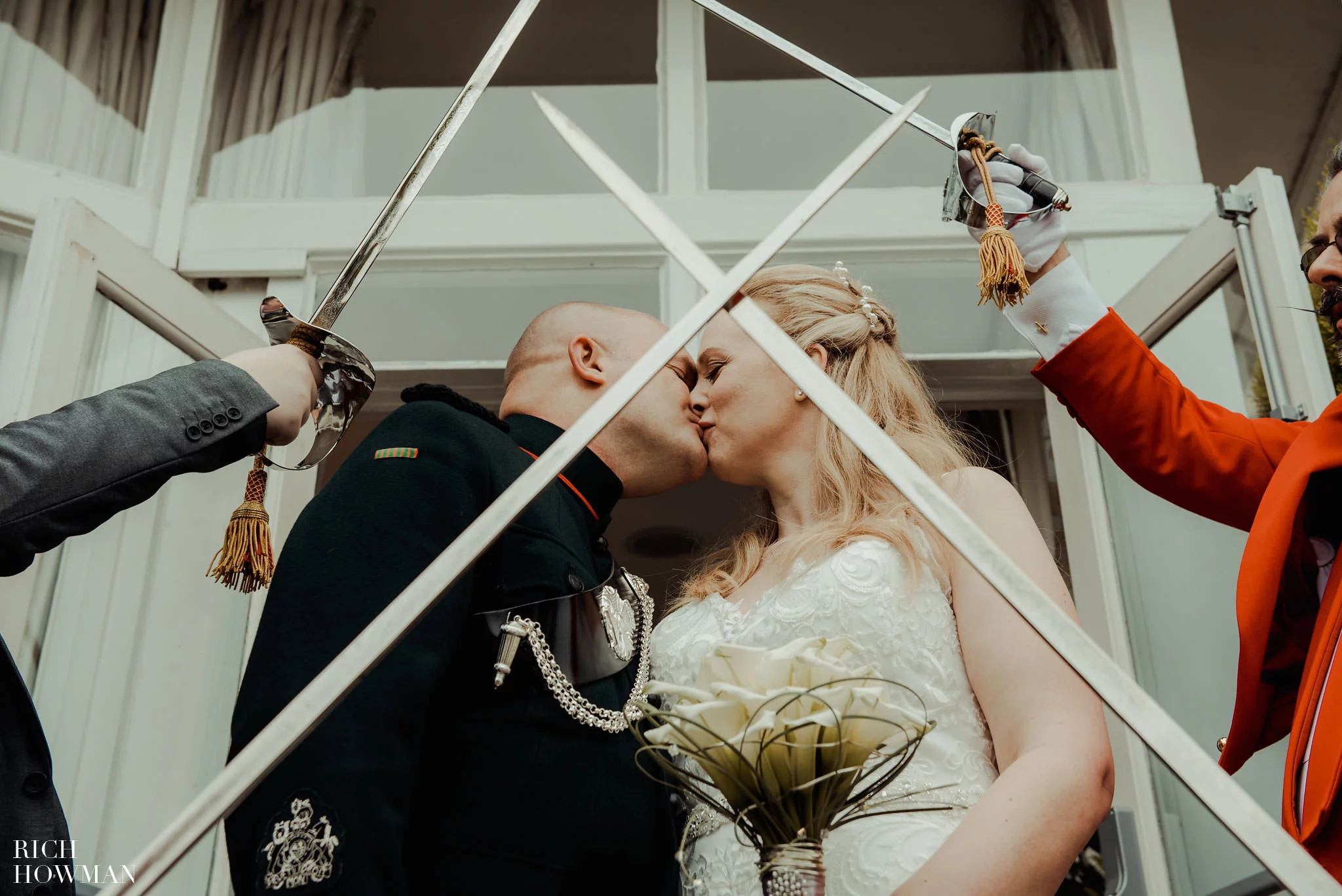 bride and groom kiss under sword archway, captured by leigh park hotel wedding photographer, rich howman