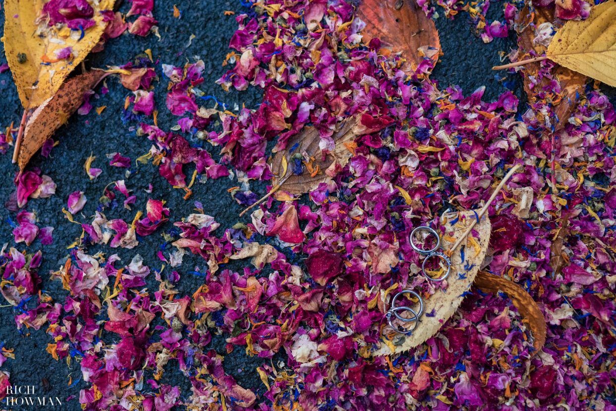 wedding rings on a pile of leaves and flower petal confetti, captured by bath wedding photographers from rich howman photography and film