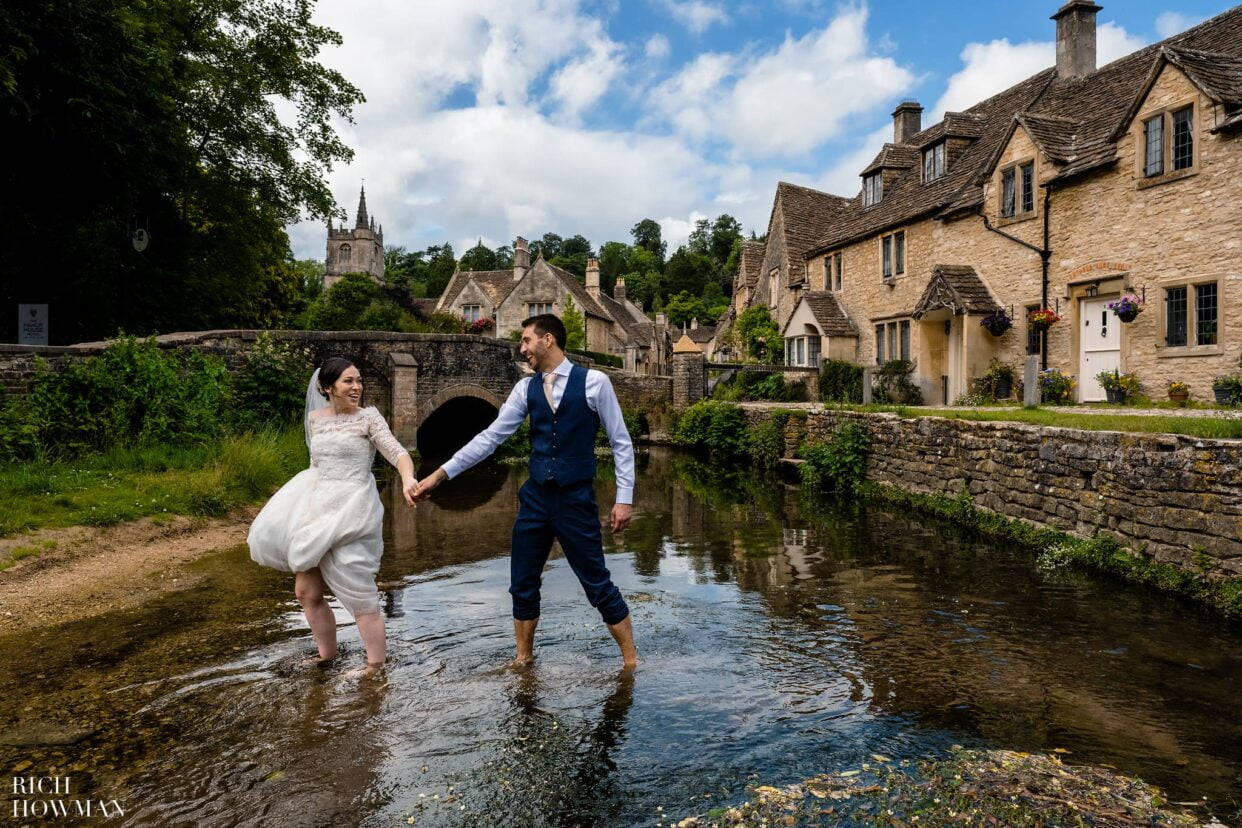 Bride and groom crossing river captured by Rich Howman, Castle Combe Wedding Photographer
