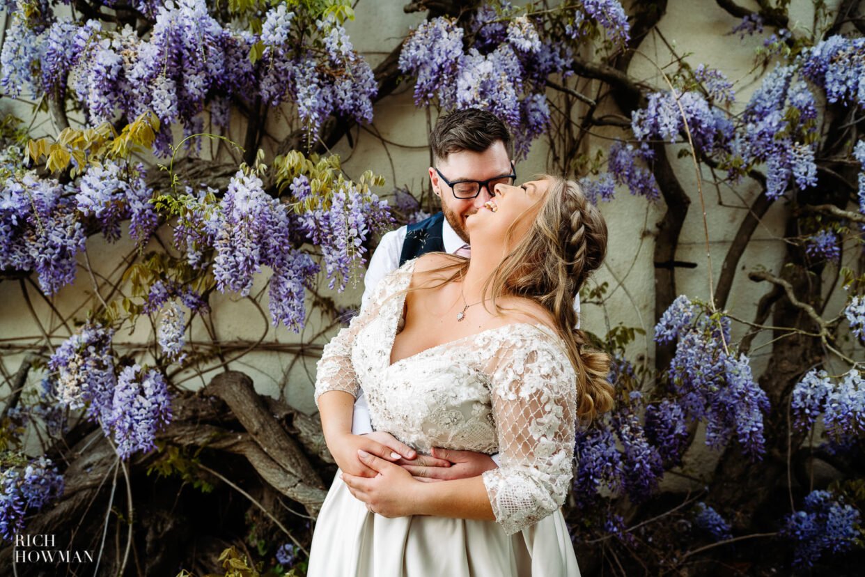 bride and groom laughing in front of wisteria wall by rockbeare manor wedding photographer, rich howman