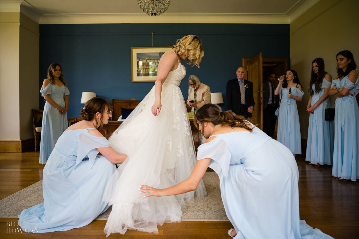coombe lodge wedding photographer captures bridemaids helping bride with her dress