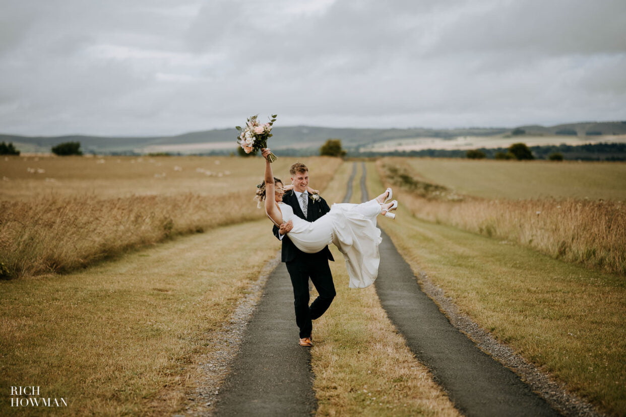 groom carries happy bride captured by chalk barn pewsey wedding photographer, rich howman