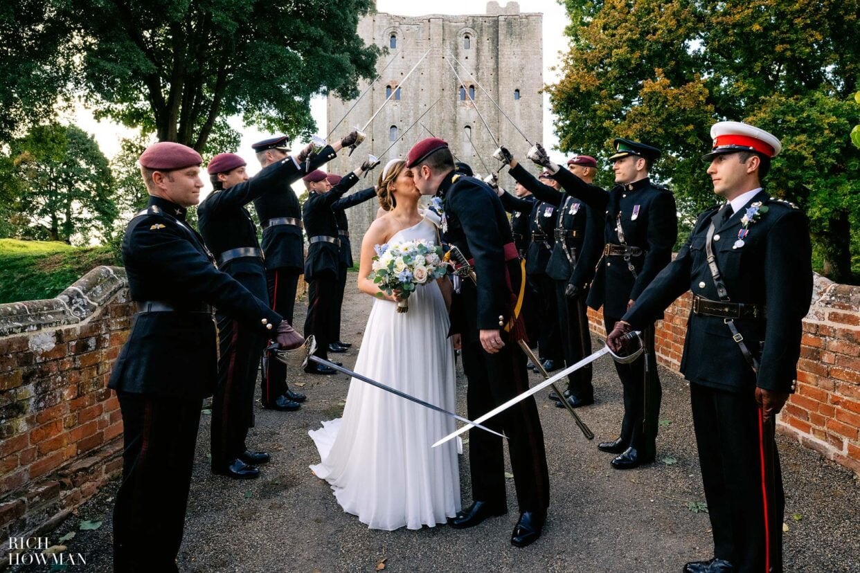 bride and groom kiss in sword arch, captured by hedingham castle wedding photographer, rich howman