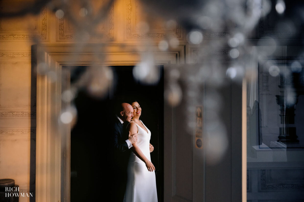 bride and groom portrait in window light, with chandelier in the foreground, captured by Clevedon Hall wedding photographer, Rich Howman