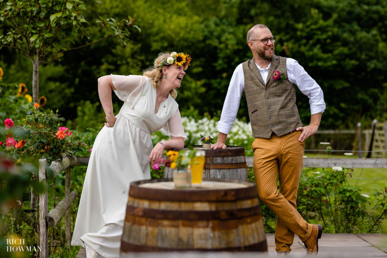 bride and groom laughing as the lean on an oak barrel, captured by lower house farm wedding photographer, Rich Howman