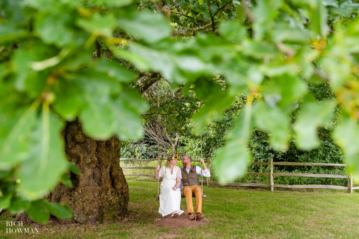 bride and groom on a woodland swing with leaves in the foreground, captured by lower house farm wedding photographer, Rich Howman