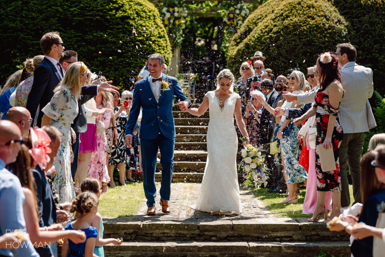 bride and groom showered with confetti after their outdoor ceremony, captured by Melksham Court wedding photographer, Rich Howman