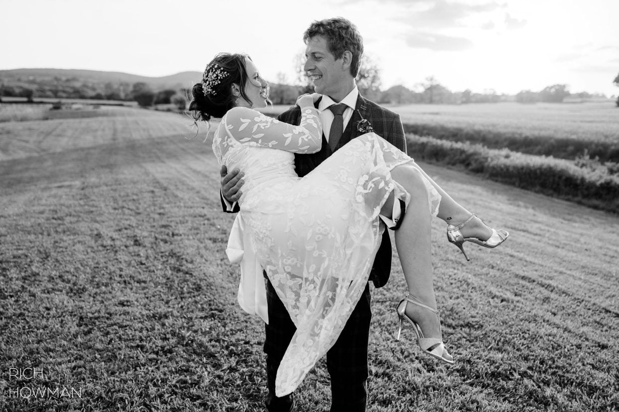 groom carrying bride in black and white photograph, captured by Quantock Lakes wedding photographer, Rich Howman