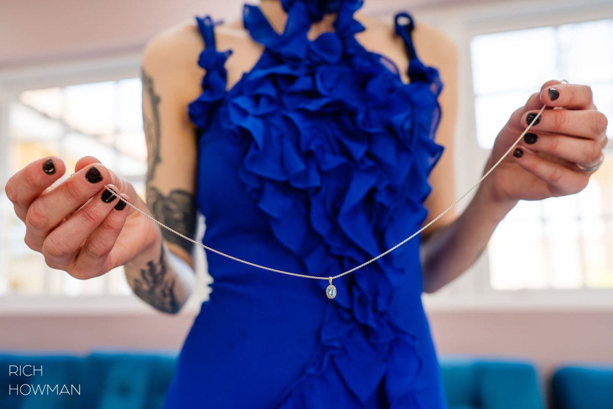 bridal necklace held by woman in blue dress, captured by Quantock Lakes wedding photographer, Rich Howman