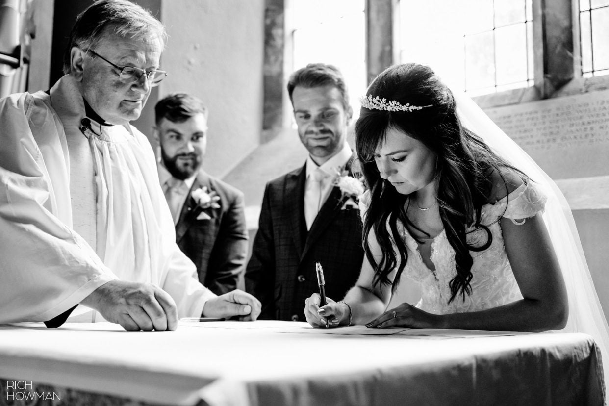 black and white image of bride and groom signing the marriage register, captured by tetbury wedding photographer, Rich Howman