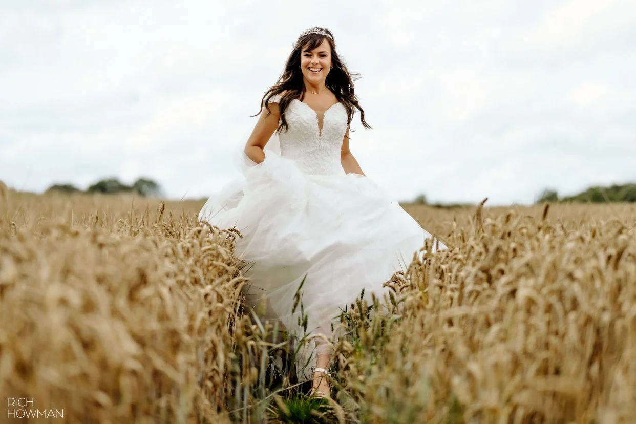 bride running through a field, captured by tetbury wedding photographer, Rich Howman