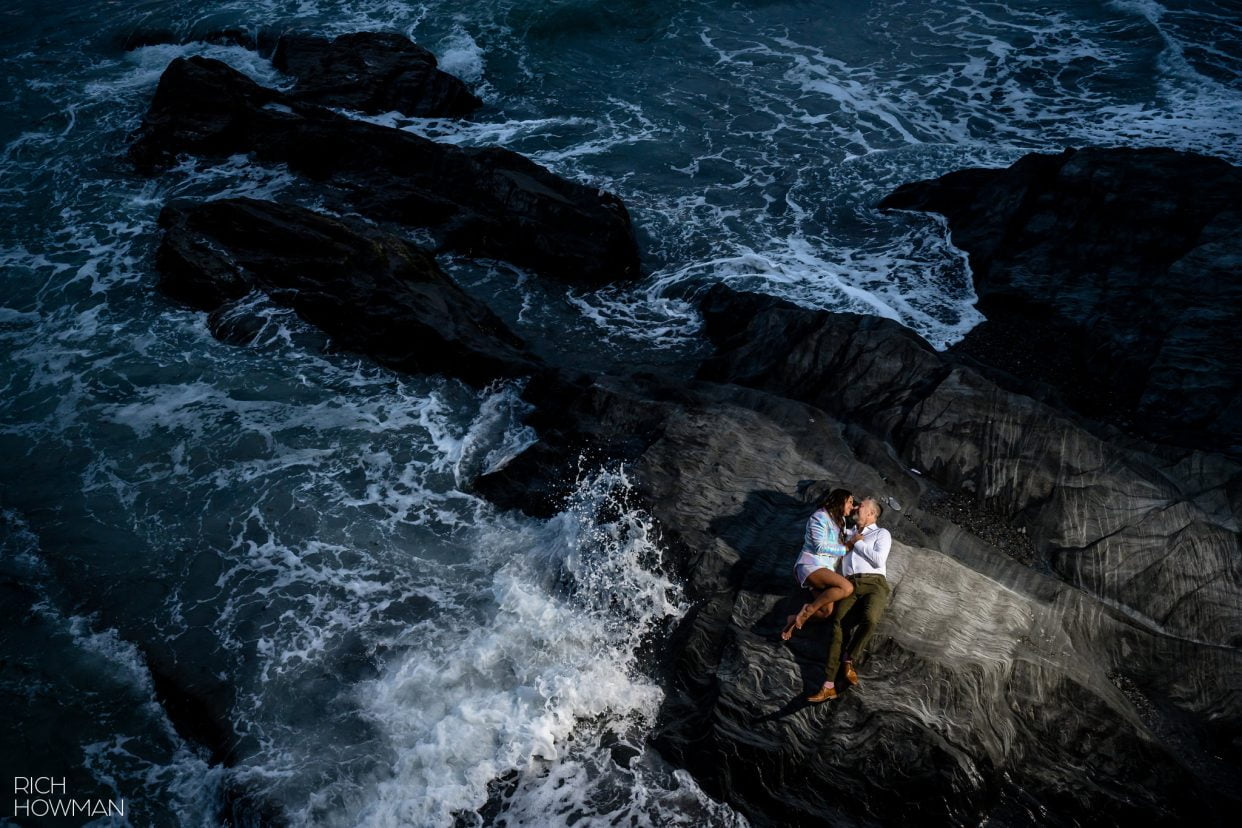 bride and groom snuggle on a rock surrounded by the waves, captured by North Devon wedding photographer, Rich Howman